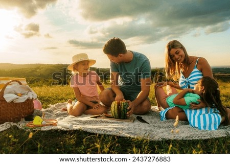 The family enjoys a day in nature, the father cuts a watermelon while the mother and daughters happily sit next to him