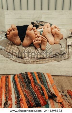 A family enjoys downtime, lying on a cushion with their bare feet entwined, showcasing a moment of domestic tranquility. Close-up of the feet of an adult and a child. Vertical frame