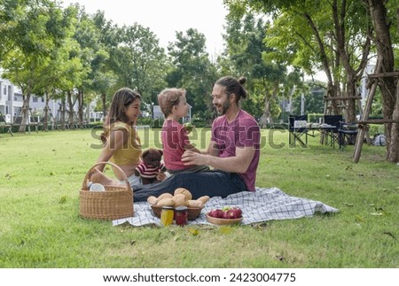 A family enjoys food together on a blanket, picnic at the park. 