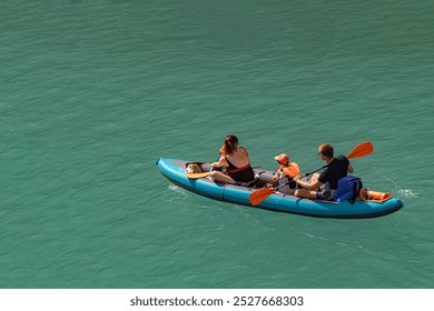 Family enjoys a trip on an inflatable 3-seater kayak or canoe on calm, turquoise water in the sunshine, with the child wearing a lifejacket; parents and child on kayak on a hot summer day in France 
 - Powered by Shutterstock