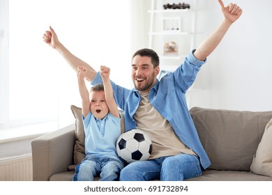 Family, Entertainment, Sport And People Concept - Happy Father And Little Son With Ball Watching Football Or Soccer Game Tv At Home