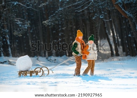 Family entertainment in winter with snow. Two happy smiling children playing pulling a sled with a snow globe. Children have fun with snowballs.