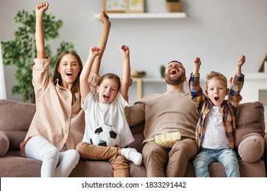 A Family Of Fans Mother Father And Children Watching A Football Match And Celebrating Goal  On TV At Home
