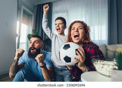Family of fans watching a football match on TV at home - Shutterstock ID 2106092696