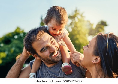 Family, father and daughter on shoulders in park with happy mom, love and summer sunshine. Young couple, baby girl or laugh together for freedom, bond and helping hand for care, backyard or garden - Powered by Shutterstock