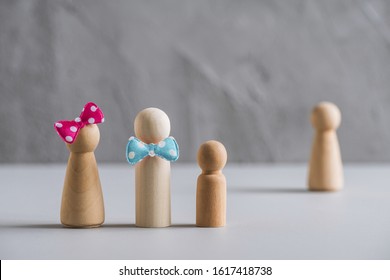 Family Father, Mother And Baby From Wooden Men In The Foreground. Woman Surrogate Mother Behind Them. Surrogacy Concept. 