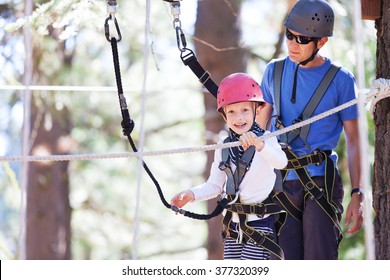 Family Of Father And Son Climbing Together At Treetop Adventure Park