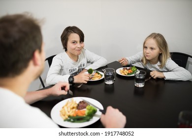 Family With Father, Son And Daughter Eating A Healthy Meal Of Steak And Vegetables At The Dinner Table.