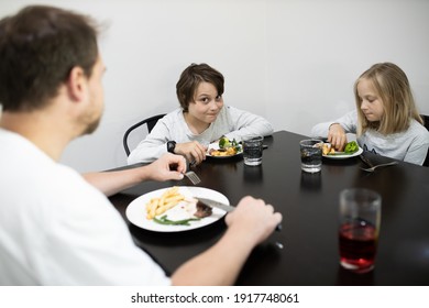 Family With Father, Son And Daughter Eating A Healthy Meal Of Steak And Vegetables At The Dinner Table.