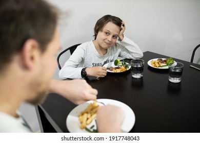 Family With Father And Son Eating A Healthy Meal Of Steak And Vegetables At The Dinner Table.