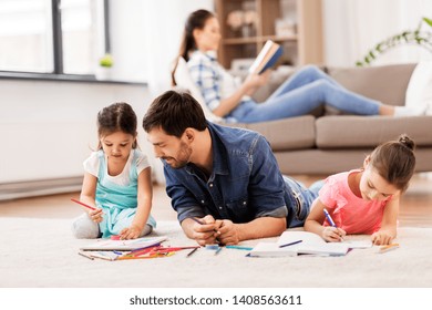 family, fatherhood and leisure concept - father spending time with his little daughters drawing in sketchbooks by crayons and lying on floor at home - Powered by Shutterstock