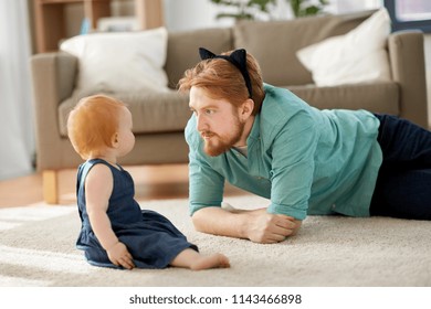 family, fatherhood and people concept - happy red haired father wearing cat ears headband playing with little baby daughter at home - Powered by Shutterstock