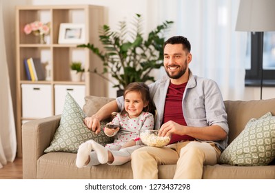 family, fatherhood and people concept - happy father and daughter with popcorn watching tv at home