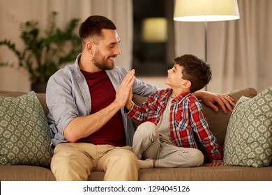 Family, Fatherhood And People Concept - Happy Father And Little Son Making High Five At Home In Evening