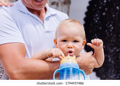 Family Feeding A Baby Boy With Water From Bottle Outside Hotel.