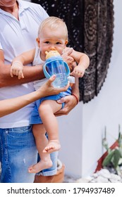 Family Feeding A Baby Boy With Water From Bottle Outside Hotel.