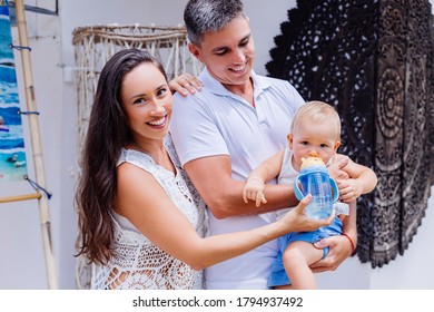 Family Feeding A Baby Boy With Water From Bottle Outside Hotel.