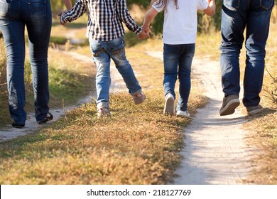 Family Feet And Legs In Jeans. Father, Mother, Son And Daughter Walking In An Urban Neighborhood. Rear View.