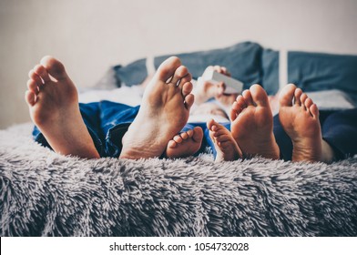 Family feet. Young family are lying on bed and playing with their feet. Mom, dad and little daughter. People are enjoying their company. Childhood and parenthood. Casual lifestyle. 