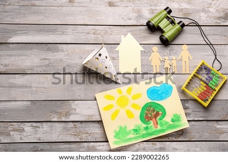 Family figure with paper house, drawing, toys and party hat on wooden background. Children's Day celebration