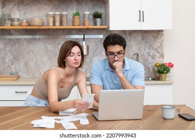 Family Financial Crisis Concept. Shocked And Stressed Couple Counting Expenses, Taxes And Debts. Laptop And Many Bills On The Table