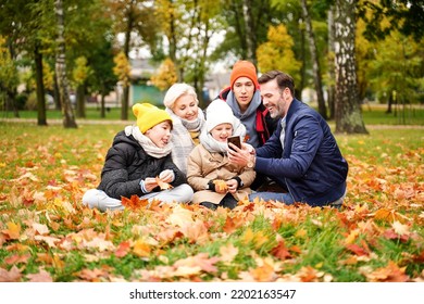 Family Of Five People Spending Time And Having Fun Together, Taking Selfie On The Mobile Phone Or Talking Online With Someone At The Autumn Golden Park. Real People Lifestyle Concept.
