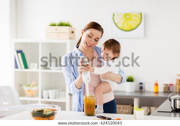 familia, comida, comida saludable, cocina y concepto de la gente - madre feliz con mezclador puré de verduras y niñita pequeña con cocina en casa