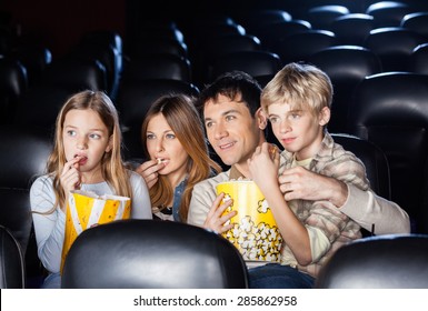 Family Of Four Eating Popcorn While Watching Film In Movie Theater