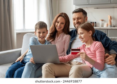 A family of four is engaged in online shopping as one of the children holds a credit card while looking at a laptop - Powered by Shutterstock