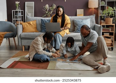 Family of four engaging in puzzle activity on floor in cozy living room filled with pillows, plants, and wall decorations - Powered by Shutterstock