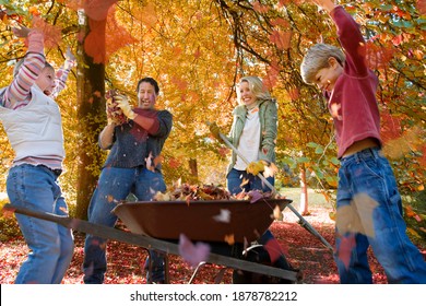 A Family Of Four Enjoying Doing Yard Work In Autumn As The Kids Are Playing With Autumn Leaves.