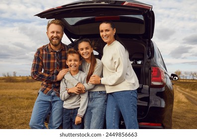 Family of four enjoying road trip on modern automobile. Happy active smiling mum, dad and little kids all together by open car trunk in autumn rural field during roadtrip in countryside.Travel concept - Powered by Shutterstock