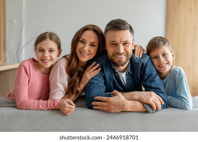 A family of four father mother daughter and son smiling and posing closely together on their living room sofa - Powered by Shutterstock