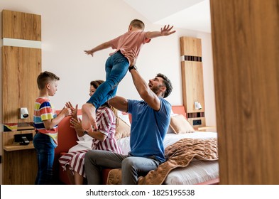 Family Of Four Having Fun And Enjoying Together At Hotel Room.