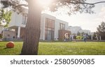 Family of four having fun tohether. Big green tree at foreground of lawn. Parents and children fooling around outside. Cheerful family spending time together near big modern house.