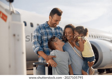 Family of four looking excited while going on a trip, standing in front of big airplane outdoors. People, traveling, vacation concept