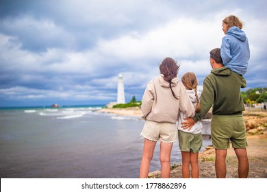 Family Of Four Near Stormy Sea Coast Look At Lighthouse