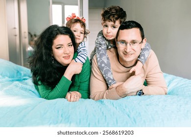 Family of four, parents with son and daughter, lying on bed in cozy bedroom, joyful and affectionate, enjoying moments indoors. Happy family relations, children playing with parents in home. - Powered by Shutterstock