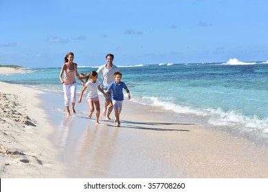 Family Of Four Running On A Sandy Caribbean Beach 