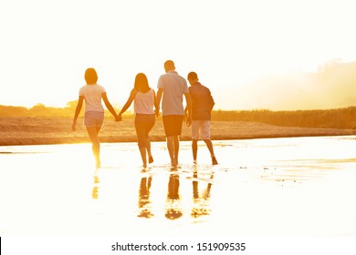 Family Of Four Silhouette By A Sunset Walking At The Beach