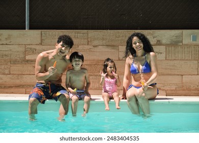 A family of four is sitting in a pool eating a popsicle looking into the camera - Powered by Shutterstock