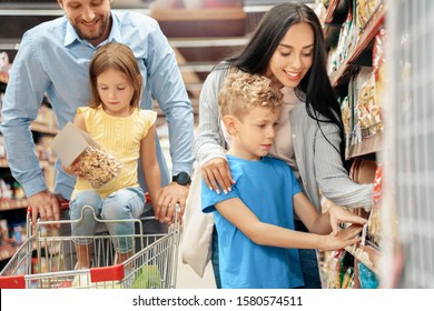 Family of four in the supermarket with cart doing daily shopping together mother and son choosing pasta concentrated while father and daughter looking at pack concerned - Powered by Shutterstock