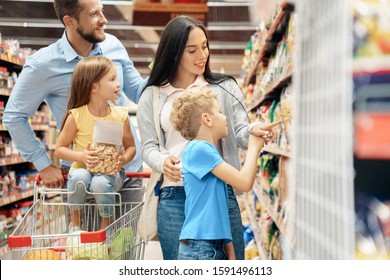 Family of four in the supermarket with cart doing daily shopping together choosing pasta for dinner concentrated smiling joyful - Powered by Shutterstock