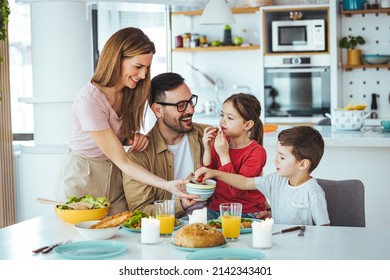 Family of four at the table, mother serves them breakfast. Everyone is happy and smiling, parents enjoy spending time with their children. A cheerful family has fun during a meal at the dining table.