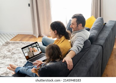 Family Of Four Using Laptop For Video Connection With Grandparents Or Family. Multiracial Mom, Dad And Two Kids Waving In Webcam Of The Laptop, Video Call, Virtual Meeting Concept