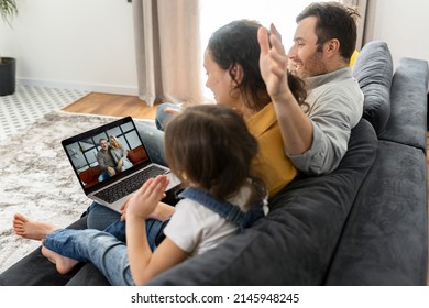 Family Of Four Using Laptop For Video Connection With Grandparents Or Family. Multiracial Mom, Dad And Two Kids Waving In Webcam Of The Laptop, Video Call, Virtual Meeting Concept