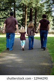 Family Of Four Walking Hand In Hand Away From The Camera. Vertically Framed Shot.