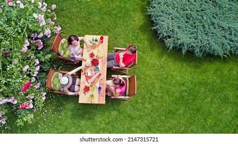 Family And Friends Eating Together Outdoors On Summer Garden Party. Aerial View Of Table With Food And Drinks From Above. Leisure, Holidays And Picnic Concept