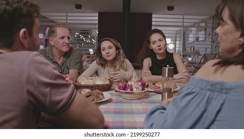 Family And Friends Gathered Outside The House At Night In Home Backyard. Group Of People Converse Sitting At Dinner Table.