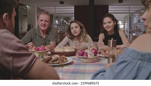 Family And Friends Gathered Outside The House At Night In Home Backyard. Group Of People Converse Sitting At Dinner Table.